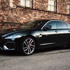 Elegancki, ciemnozielony Jaguar XF na tle ceglanej ściany. Czy jaguar XF to dobre auto? Wygląda na to, że tak!