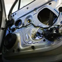 Wnętrze drzwi samochodu z widocznym mechanizmem podnośnika do szyb, głośnikiem i przewodami.