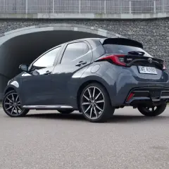 Szary hatchback Toyota Yaris z przyciemnianymi szybami i sportowym dyfuzorem. Widoczny pas tylny pojazdu z charakterystycznymi światłami i spoilerem.