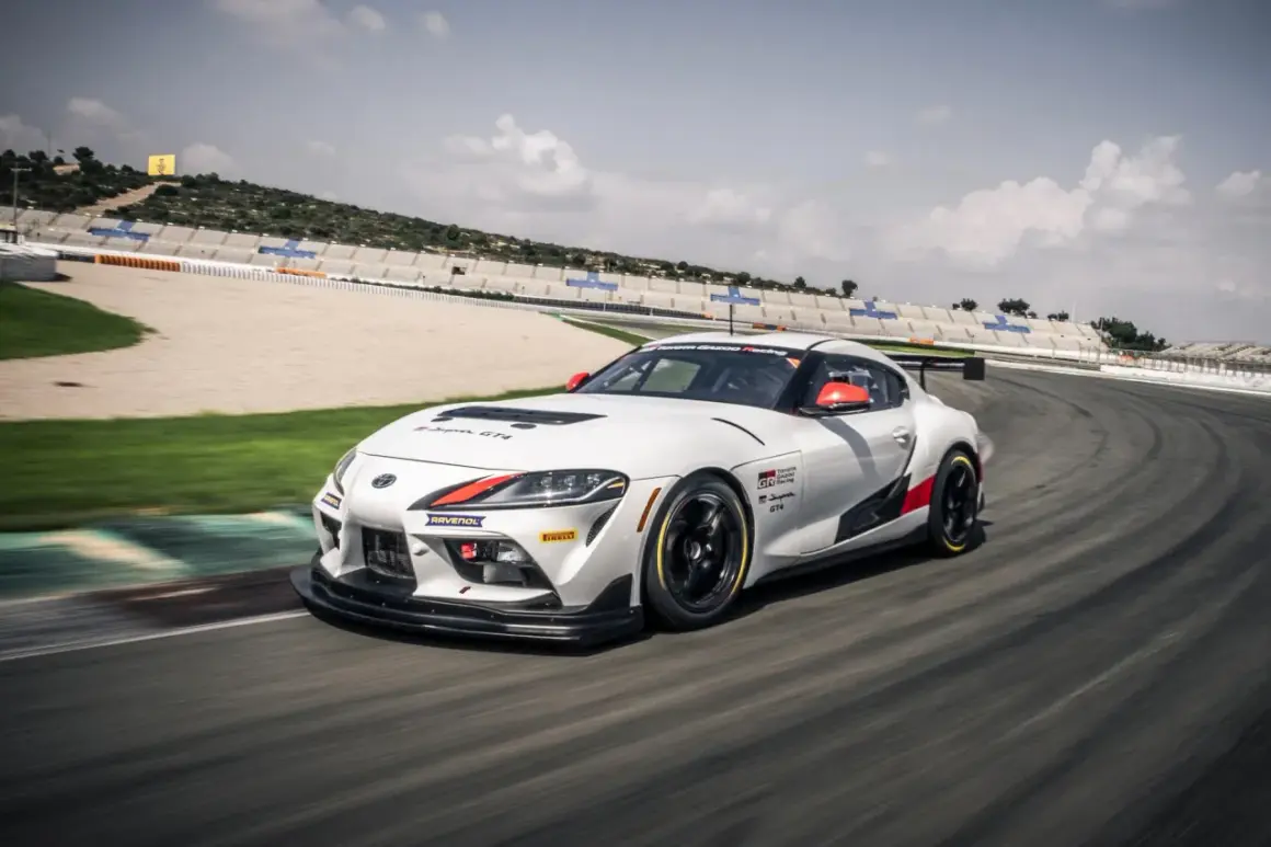 Biała, sportowa nowa Toyota Supra GT4 z czerwonymi akcentami pędzi po torze wyścigowym.
