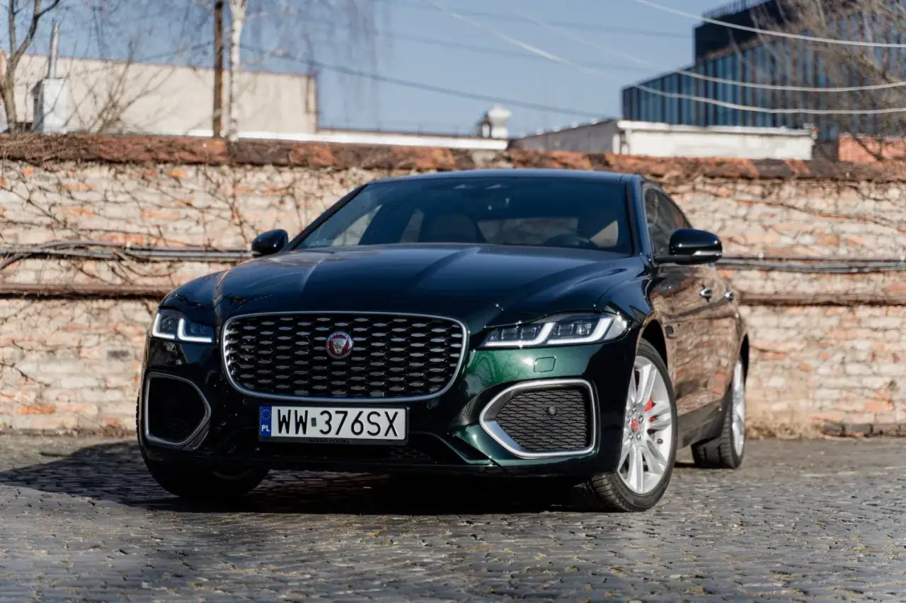 Elegancki, ciemnozielony Jaguar XF na brukowanej ulicy. Czy jaguar XF to dobre auto? Ten model z pewnością robi wrażenie.