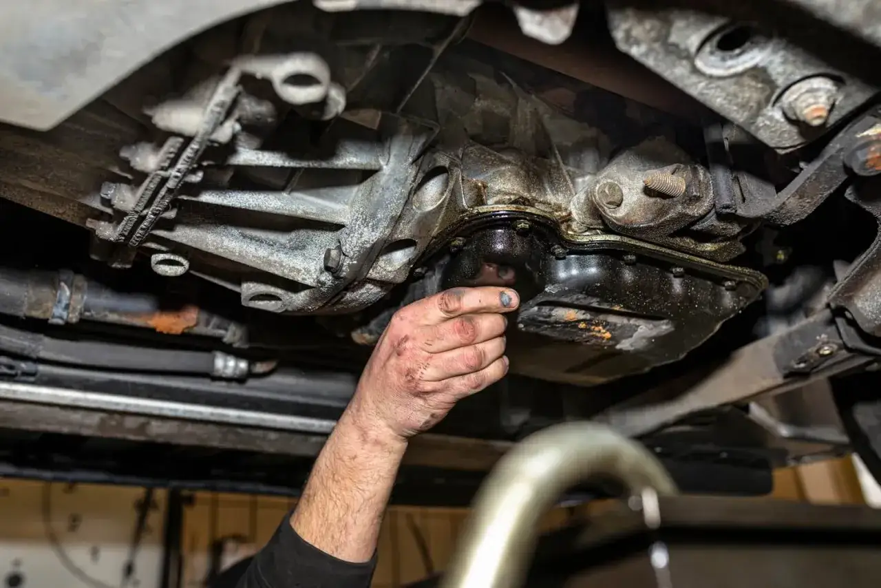 Mechanik sprawdza, gdzie jest miska olejowa w samochodzie, widoczna pod skrzynią biegów, z widocznymi śladami wycieku oleju.